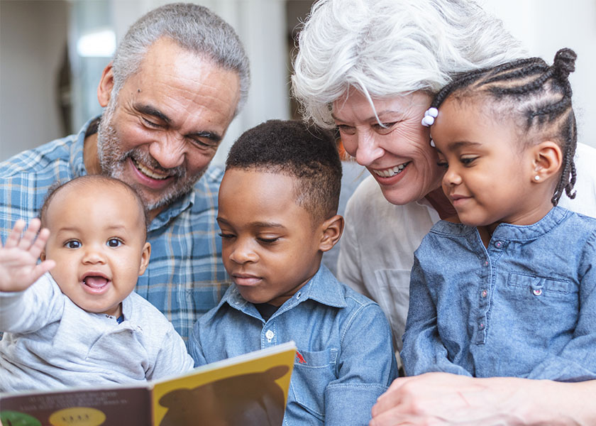 Grandpa and grandma sitting with three young grandchildren reading a children’s book. Leaving a legacy.